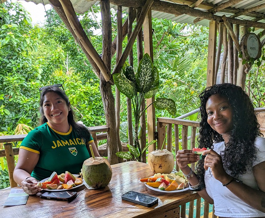 two young women sitting on a deck enjoying big plates of fresh fruit